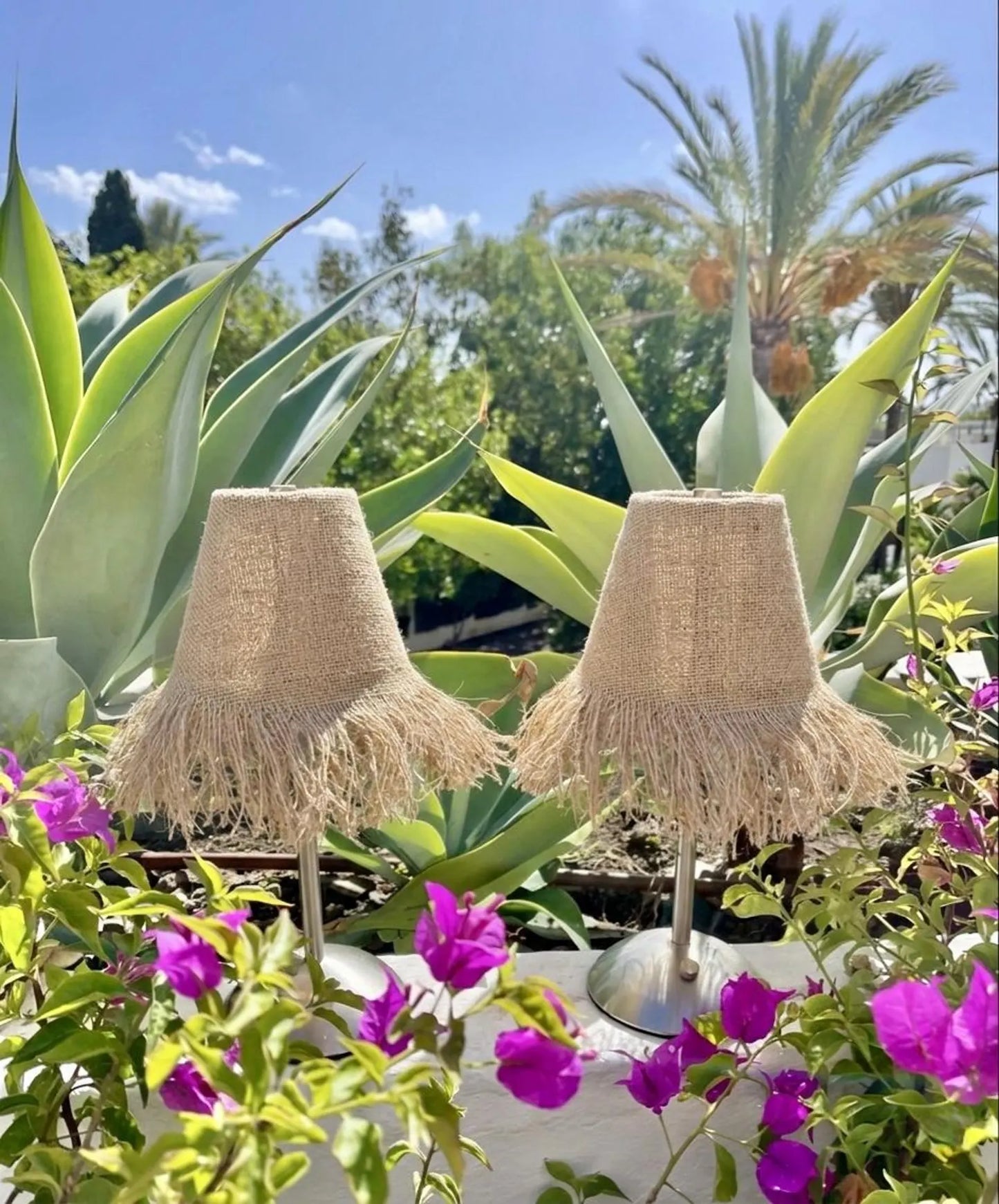 Pair of handcrafted burlap fringe lamp shades on cordless bases styled at a luxury beach club with tropical palms and ocean views.