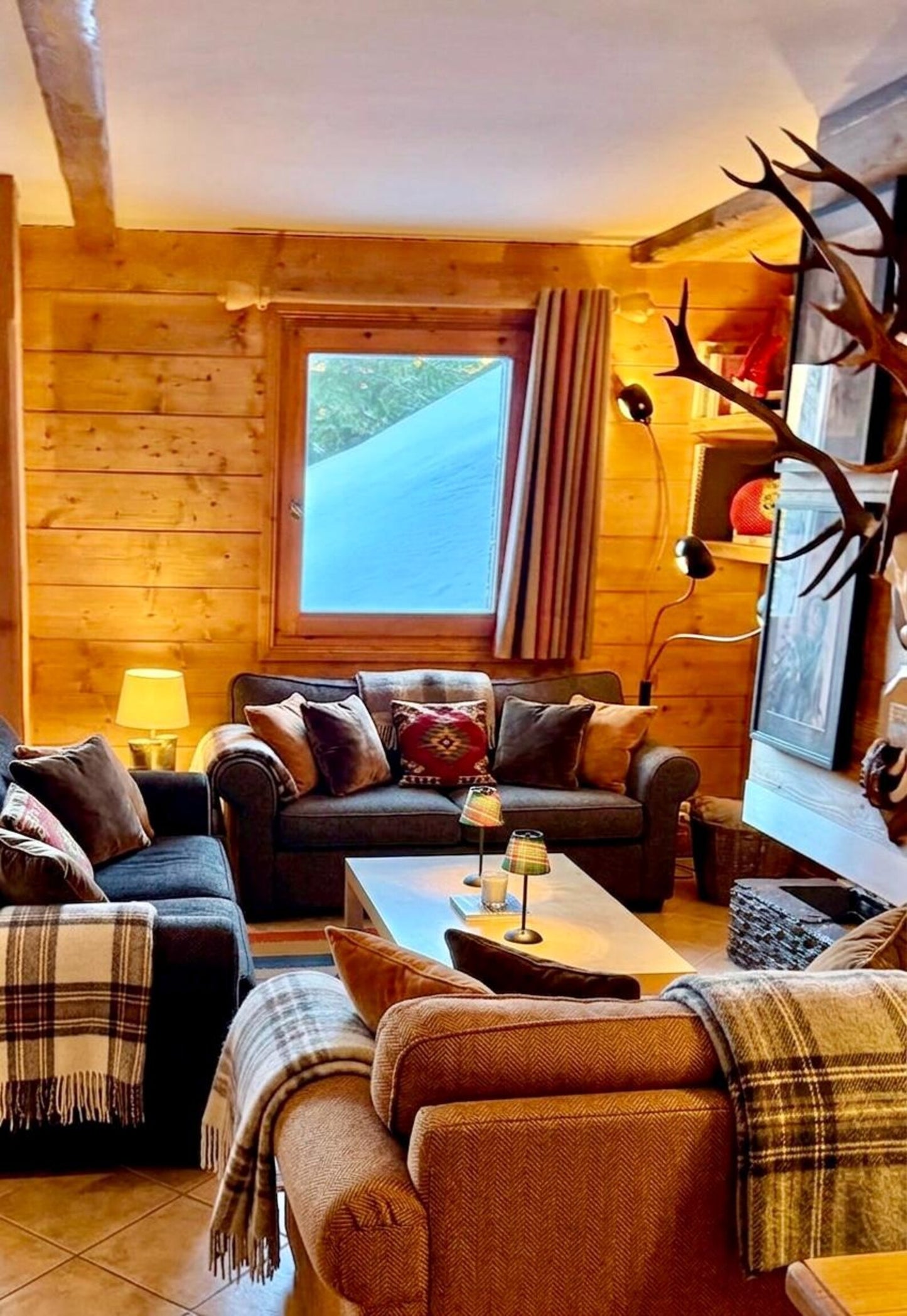Luxury mountain lodge living room with panoramic snow views featuring an Aspen plaid shade for a cordless lamp on a central coffee table.