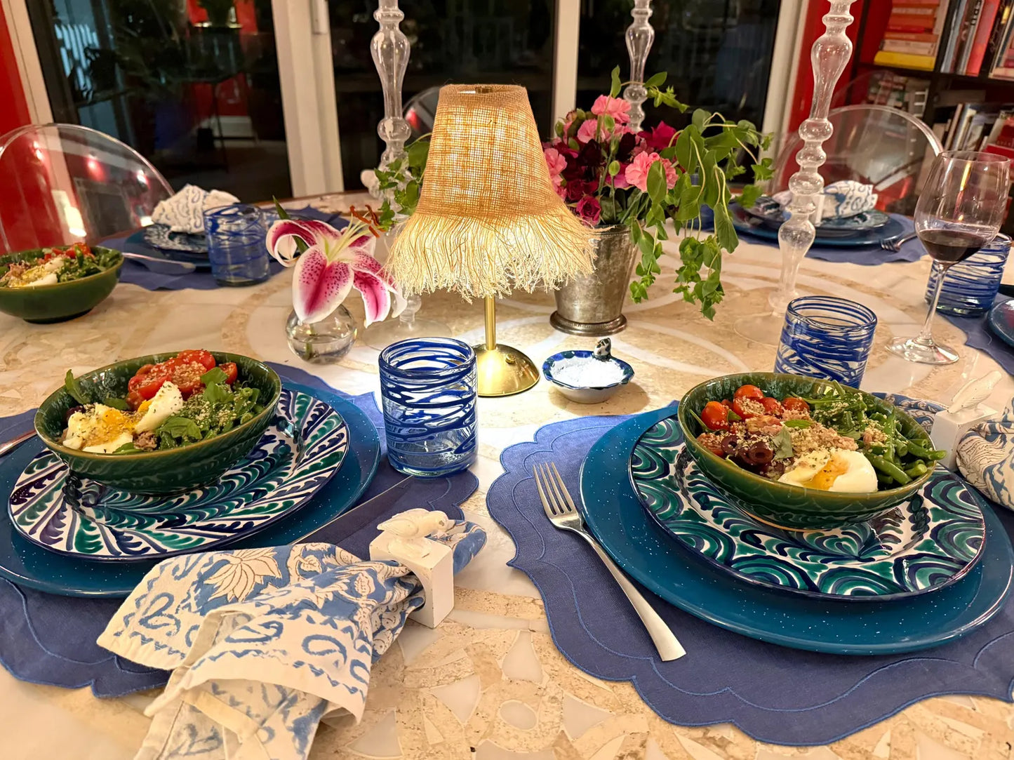 Elegant tablescape featuring a gold cordless LED lamp with a fringe shade, blue and white placemats, hand-painted plates, ikat print napkins, and colorful salad bowls—perfect for dinner parties or holiday entertaining