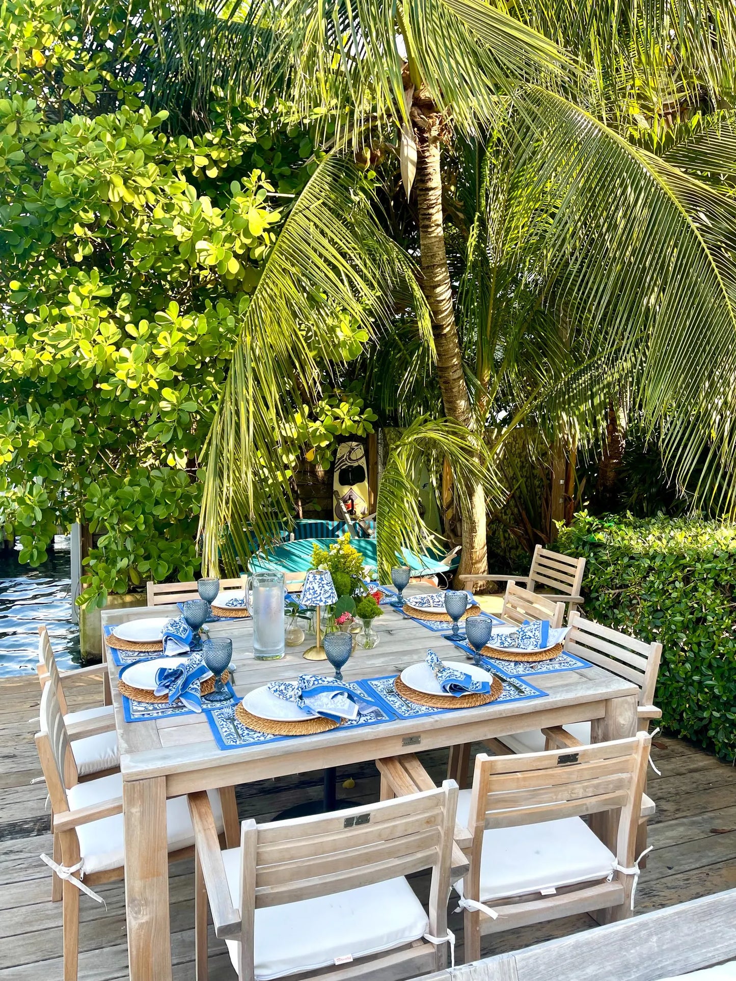 Curated outdoor dining table featuring blue seashells lampshades on cordless lamps under lush tropical palms.