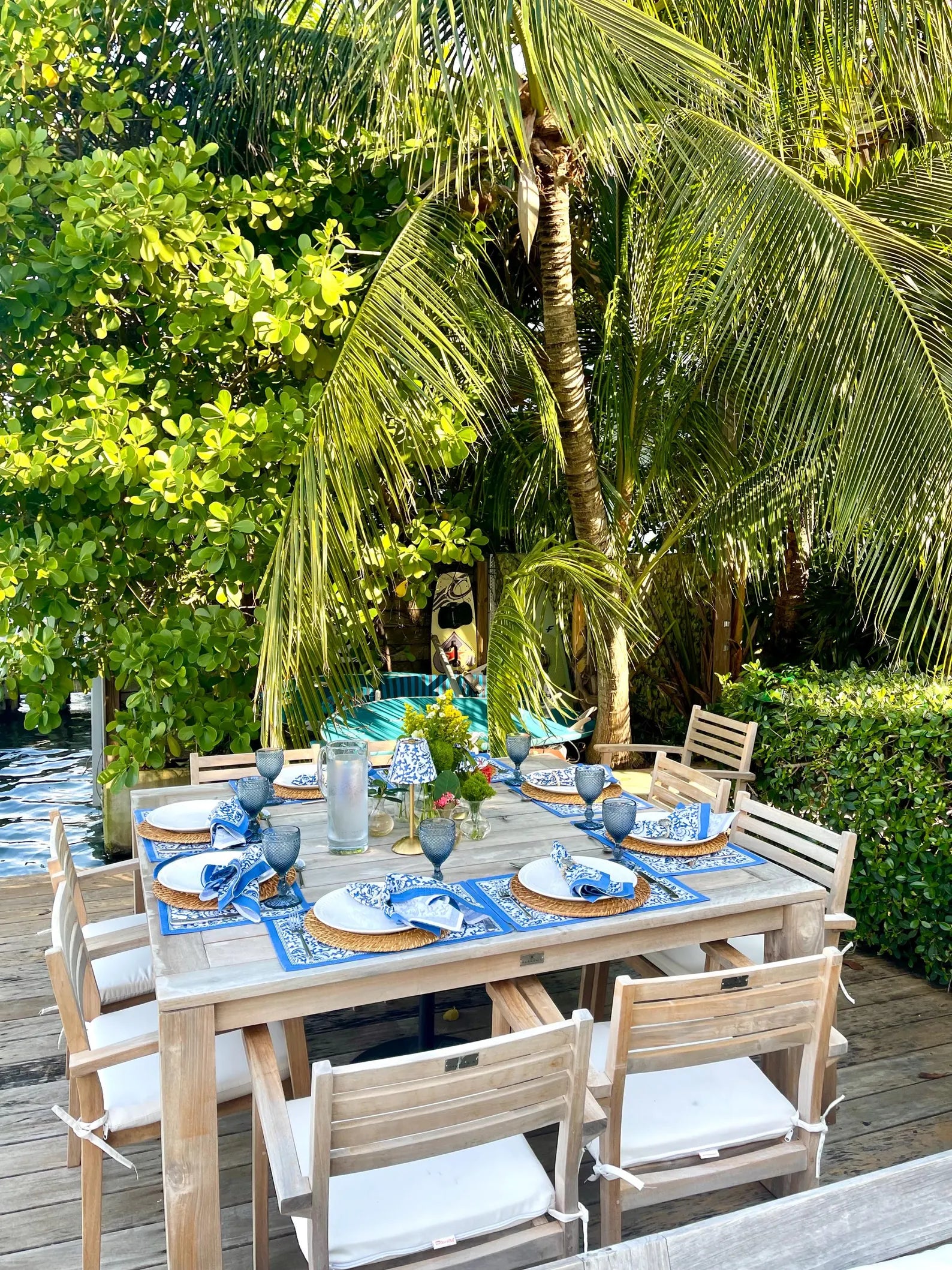 Curated outdoor dining table featuring blue seashells lampshades on cordless lamps under lush tropical palms.