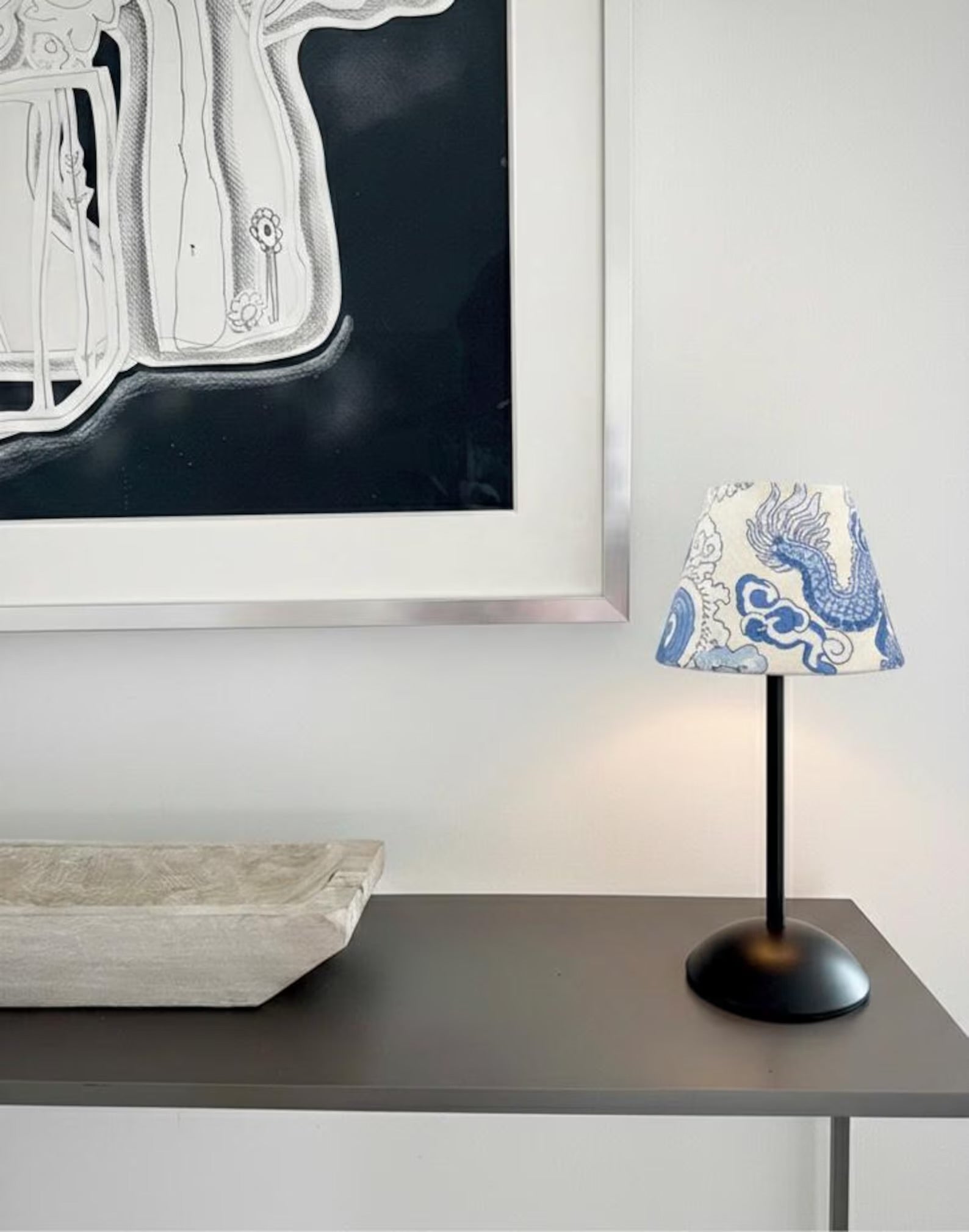 Blue dragon motif blockprint lampshade on a black cordless base styled on a modern console with architectural decor.