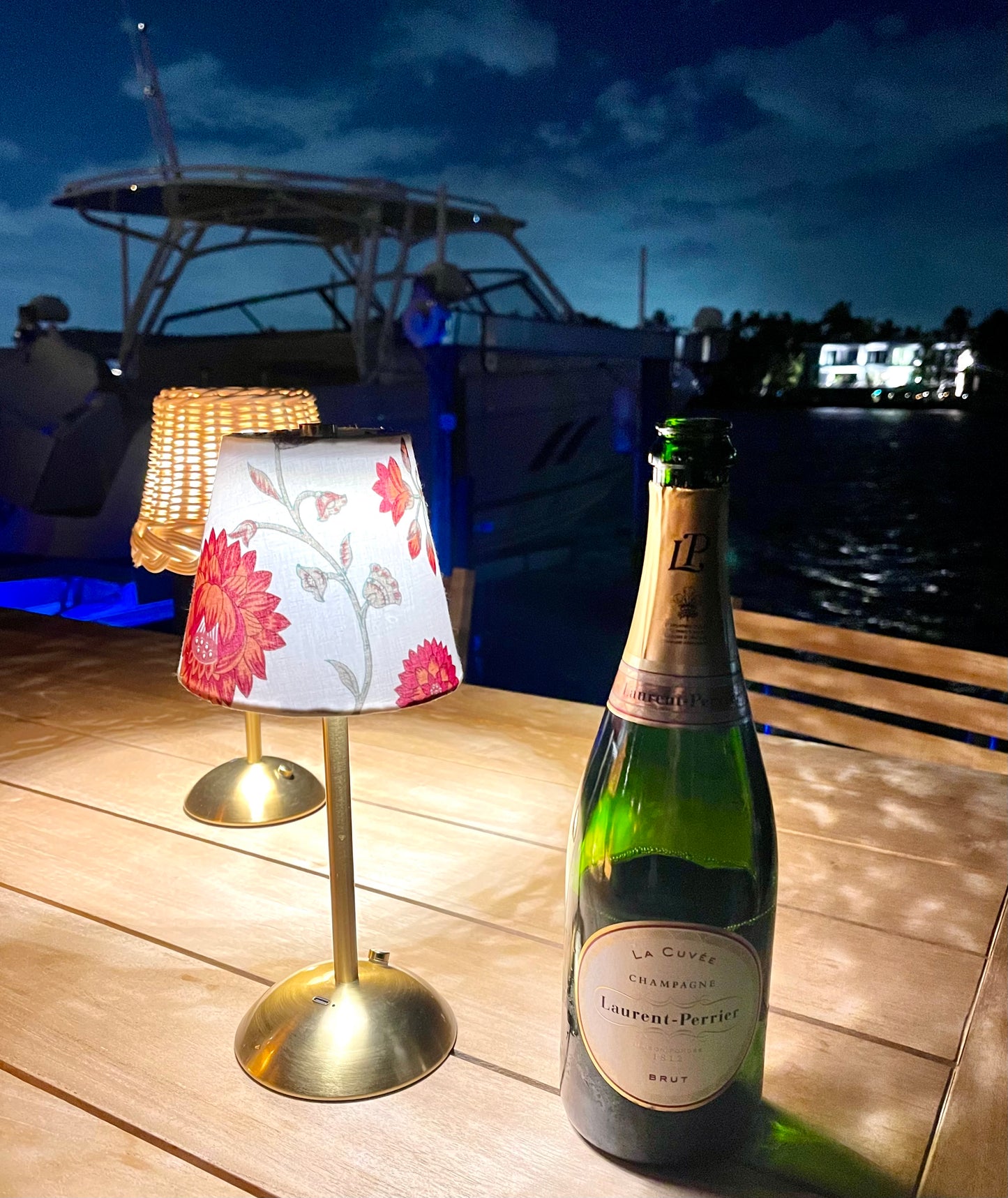 Outdoor Use: The Nandina Lamp Shade on a gold cordless lamp, styled outdoors with a champagne bottle, highlighting its use for outdoor dining and entertaining.