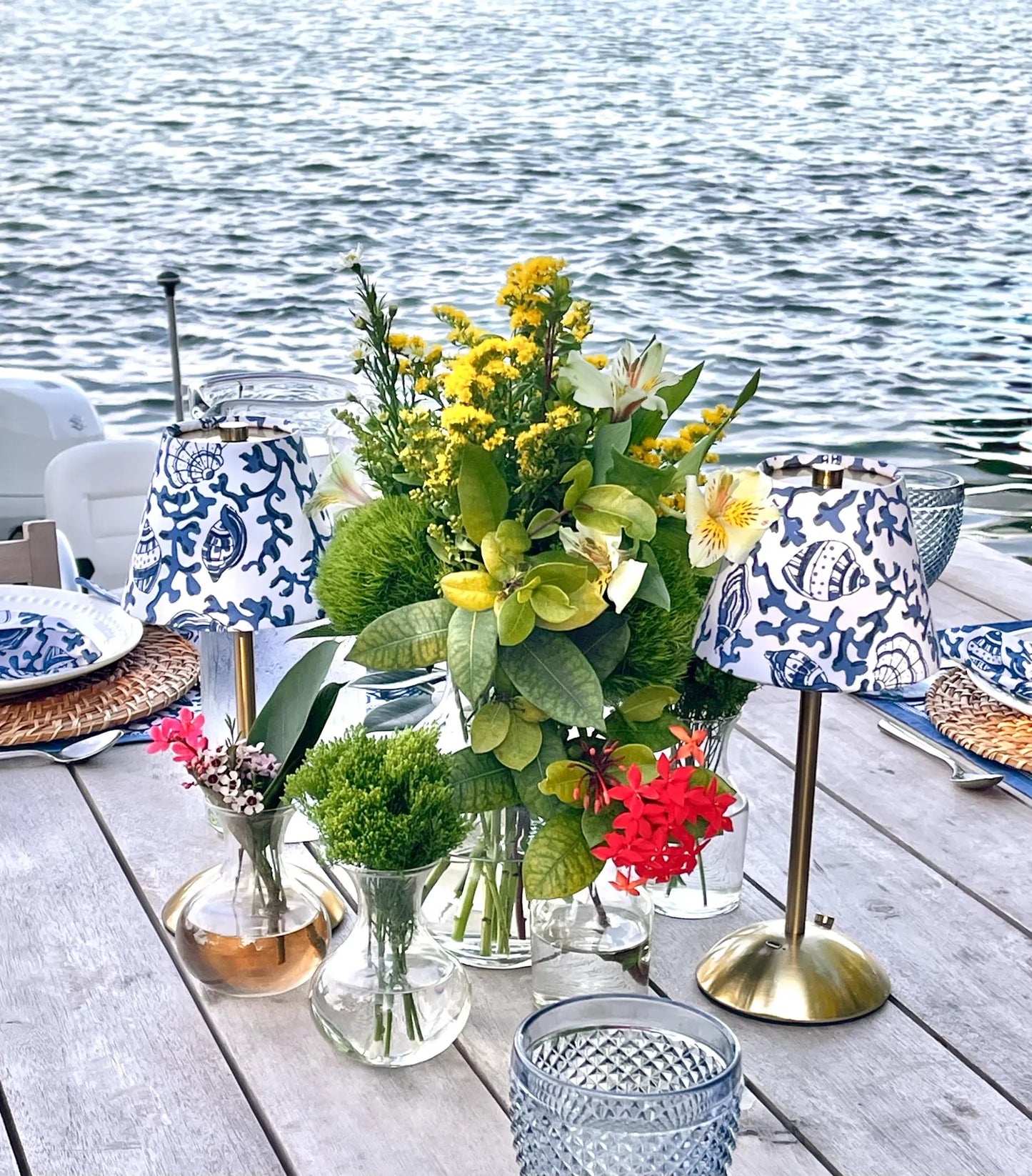 Pair of blue seashells lamp shades on cordless lamp providing ambient light for a waterfront dinner on a wooden terrace.