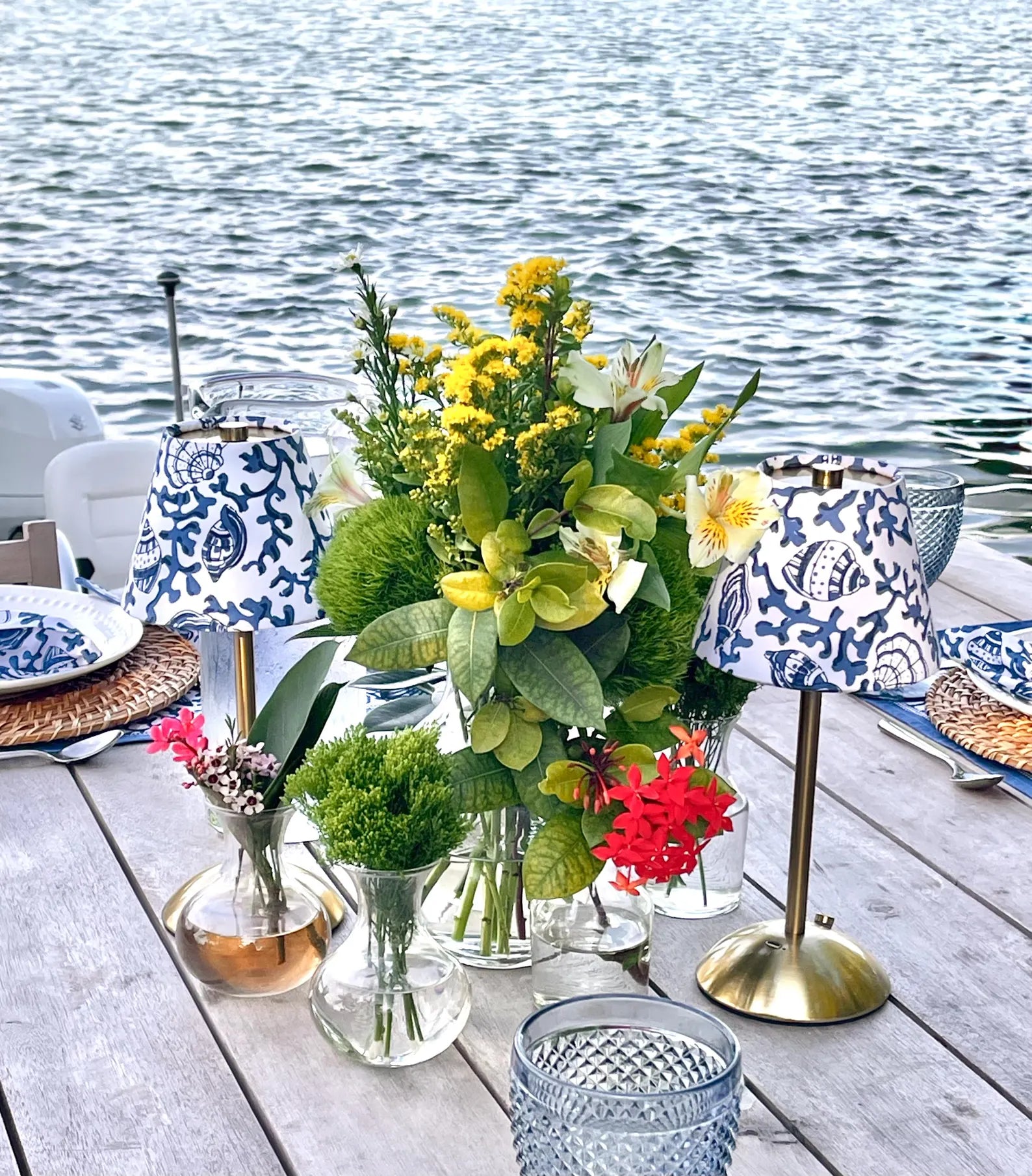 Pair of blue seashells lamp shades on cordless lamp providing ambient light for a waterfront dinner on a wooden terrace.