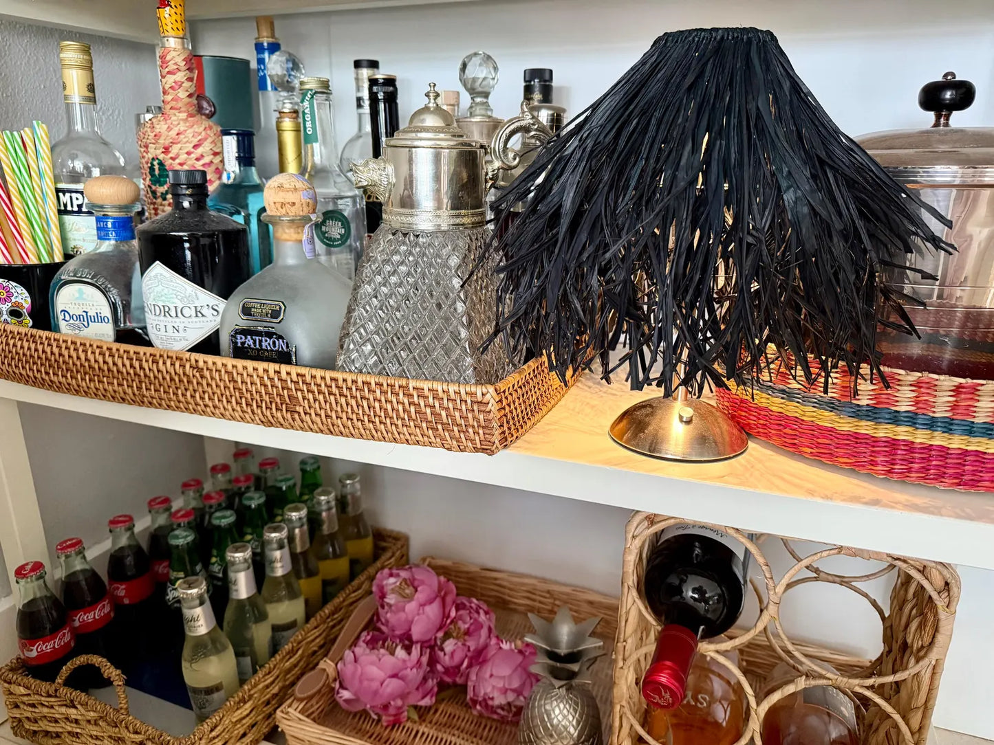 Boutique black raffia lamp shade on a woven cordless lamp base styled on an archival bar shelf with spirits.