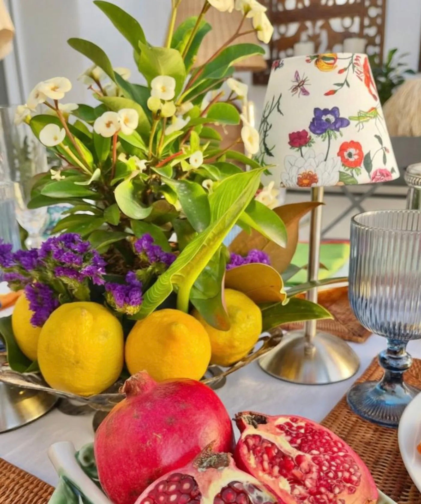 The Botánica cordless lamp shade styled on a silver base as part of a vibrant Mediterranean tablescape with lemons and pomegranates.