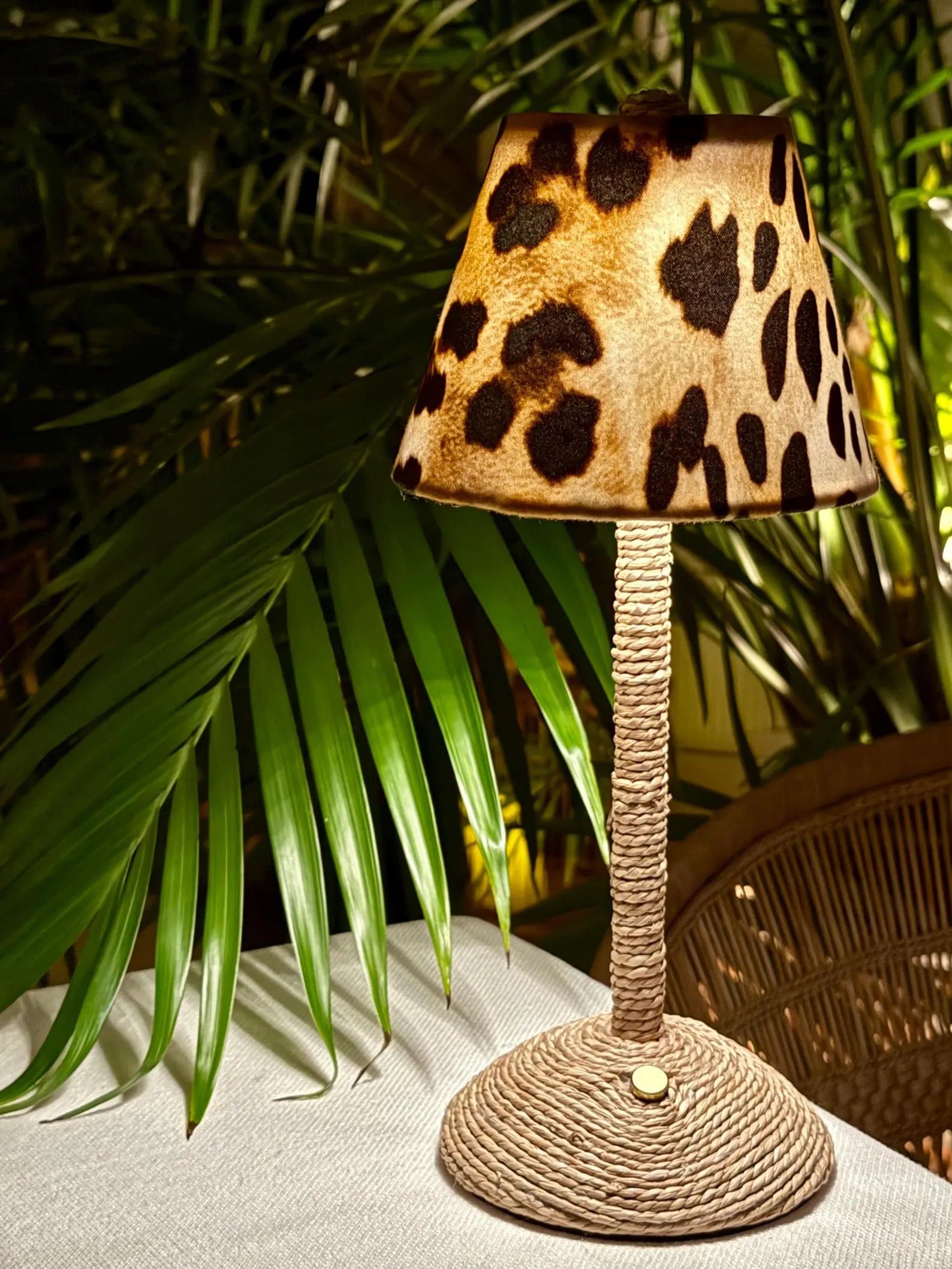 Boutique leopard print lamp shade on a gold cordless lamp base styled outdoors with tropical palms.
