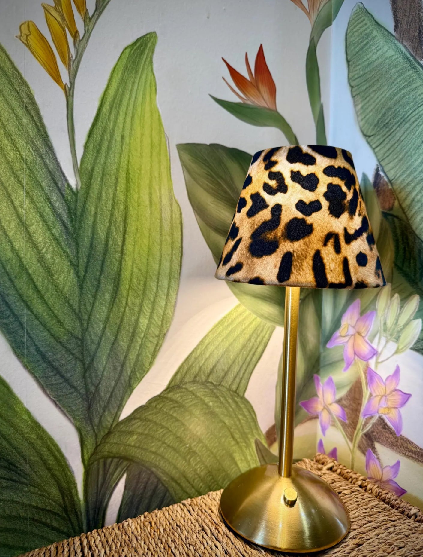 Boutique leopard print lamp shade on a gold cordless lamp base styled with a tropical wallpaper
