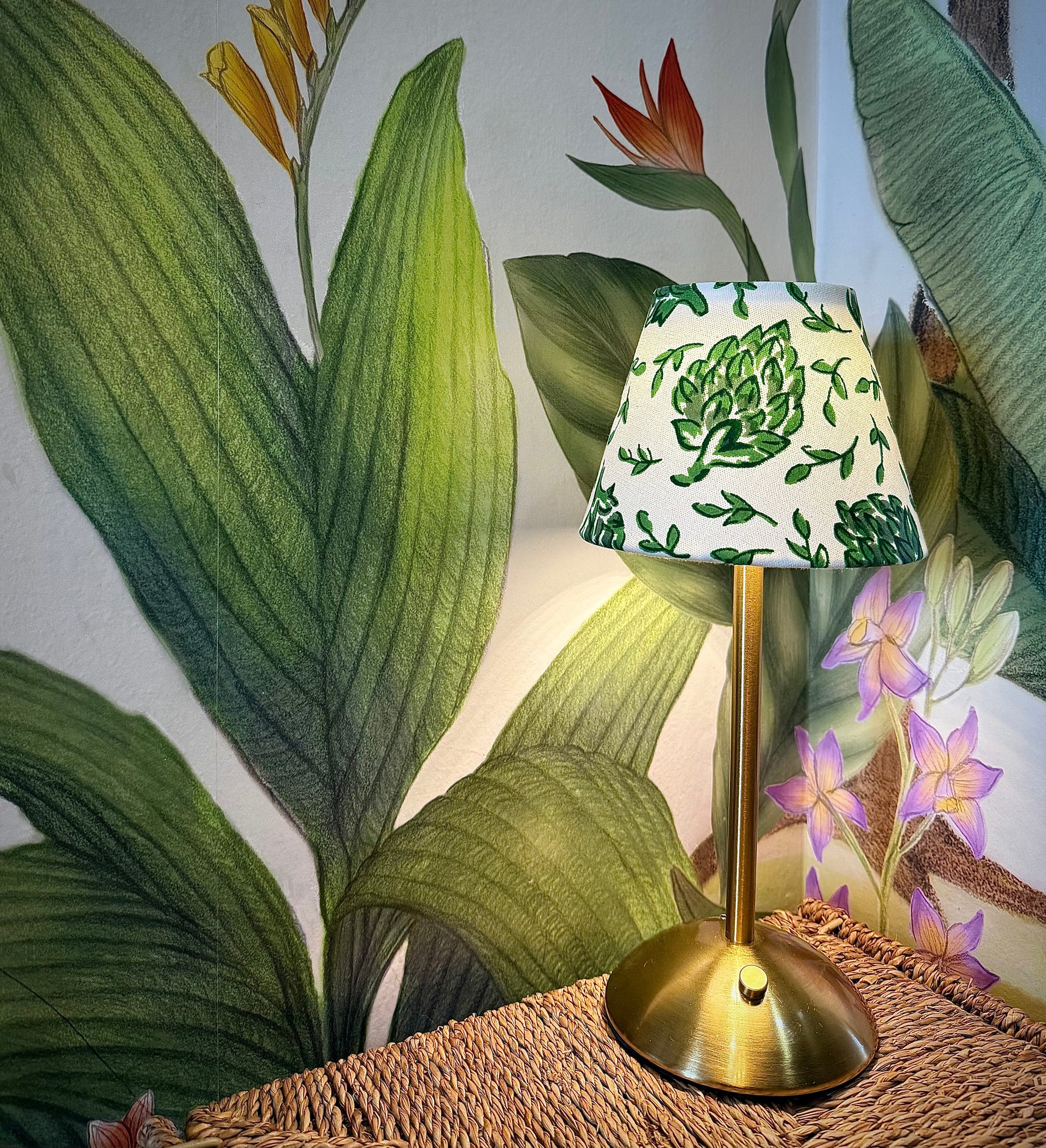 Boutique artichoke shade on a gold cordless base against a textured botanical wallpaper background.