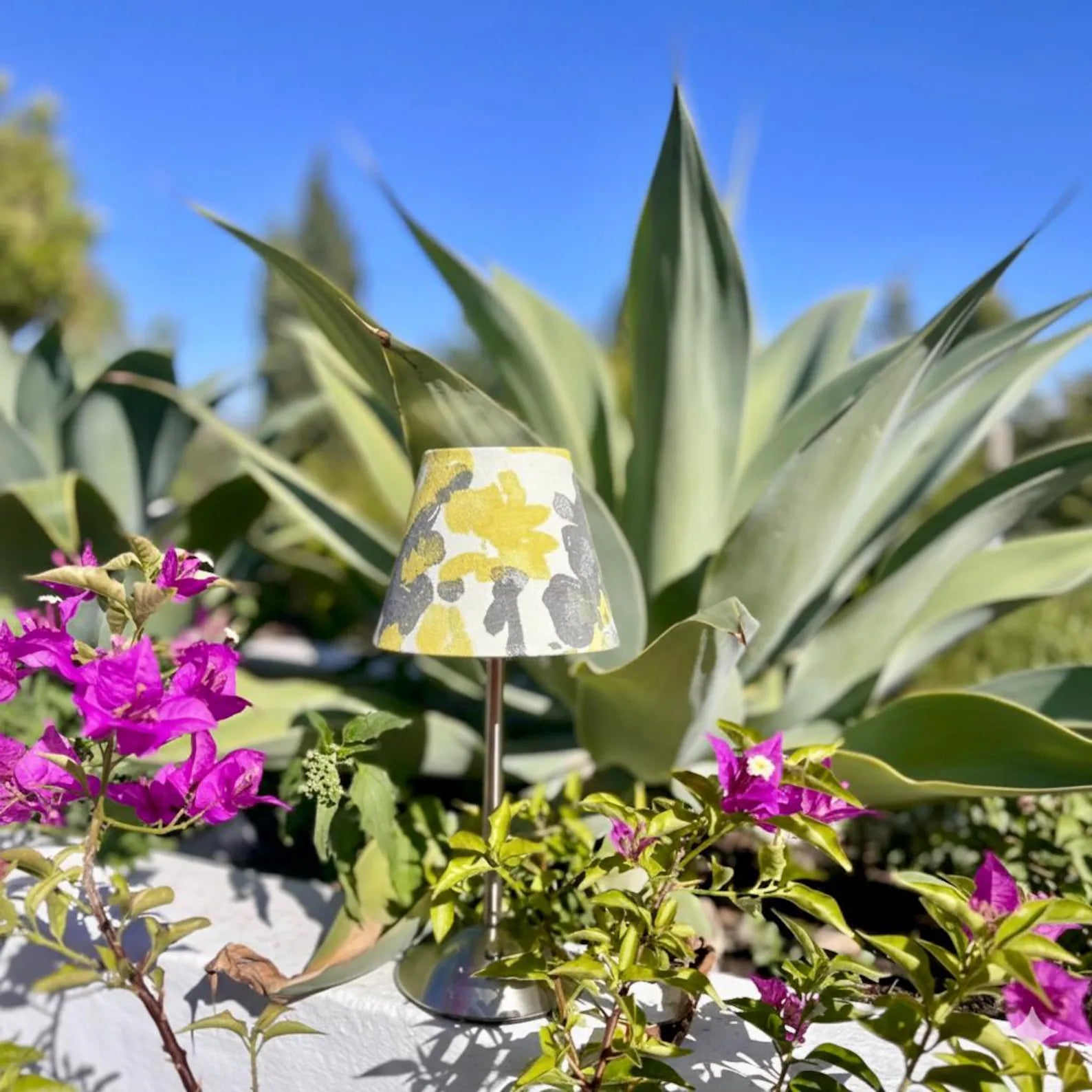 Ochre abstract shade on a silver cordless lamp styled outdoors with desert agaves and vibrant bougainvillea.