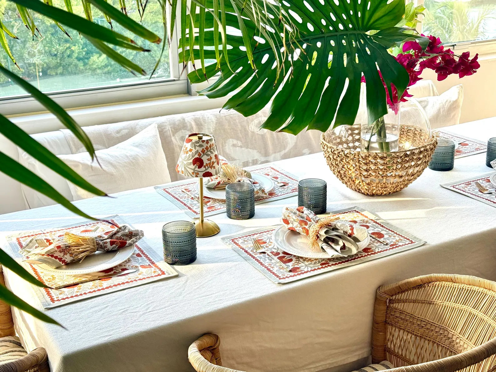 Table setting featuring Marigold floral lamp shades on a cordless table lamp, rattan chairs, and a tropical centerpiece, styled for a bright and cheerful dining look