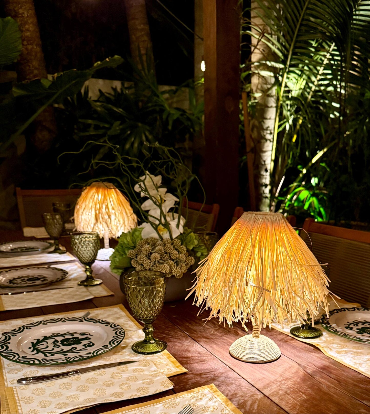Night tablescape with raffia shades on cordless lamps providing fire-safe ambient lighting for outdoor garden dining.