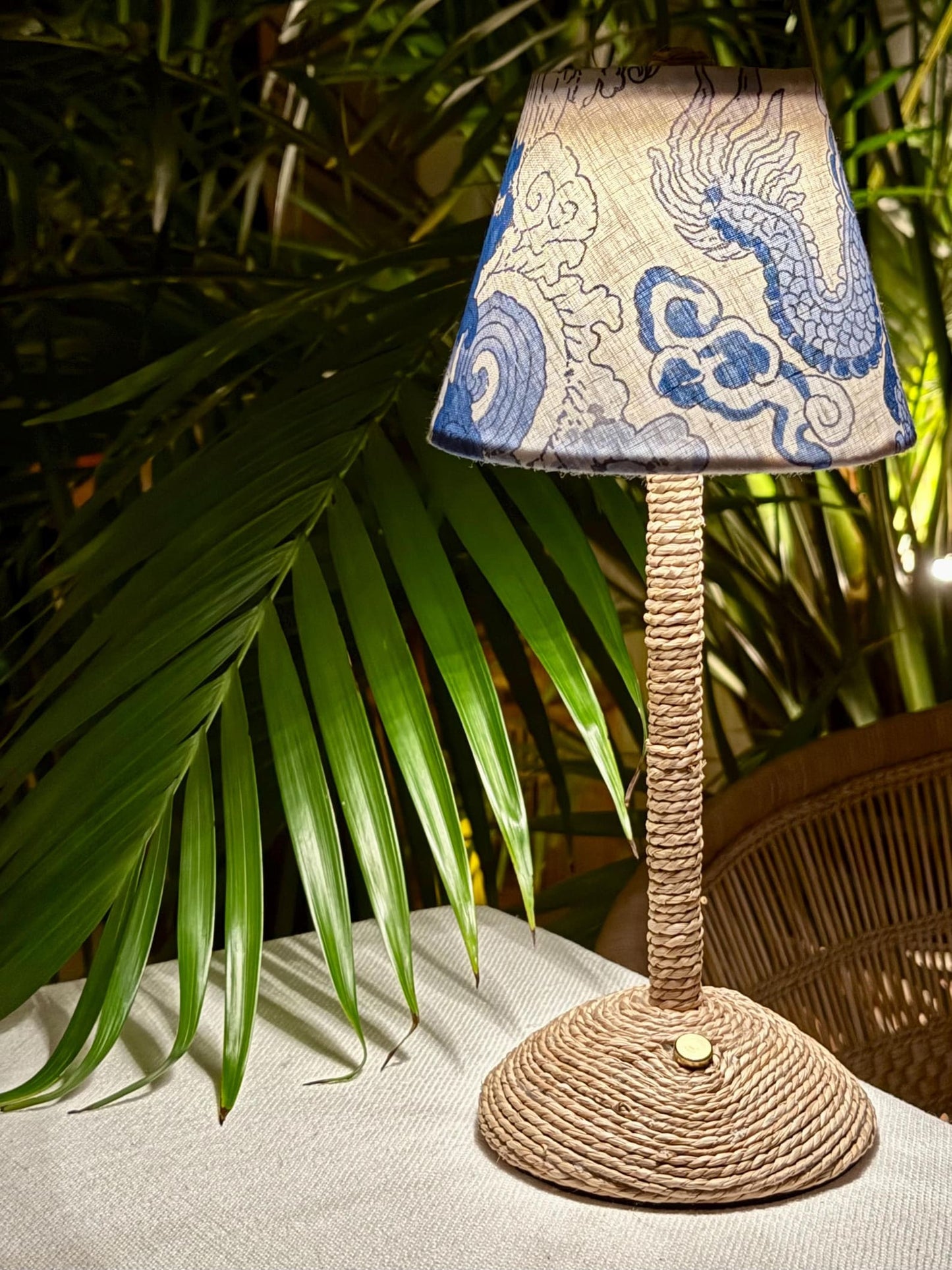 Boutique blue dragon linen shade on a woven base styled with tropical palm shadows for island luxe interior decor.