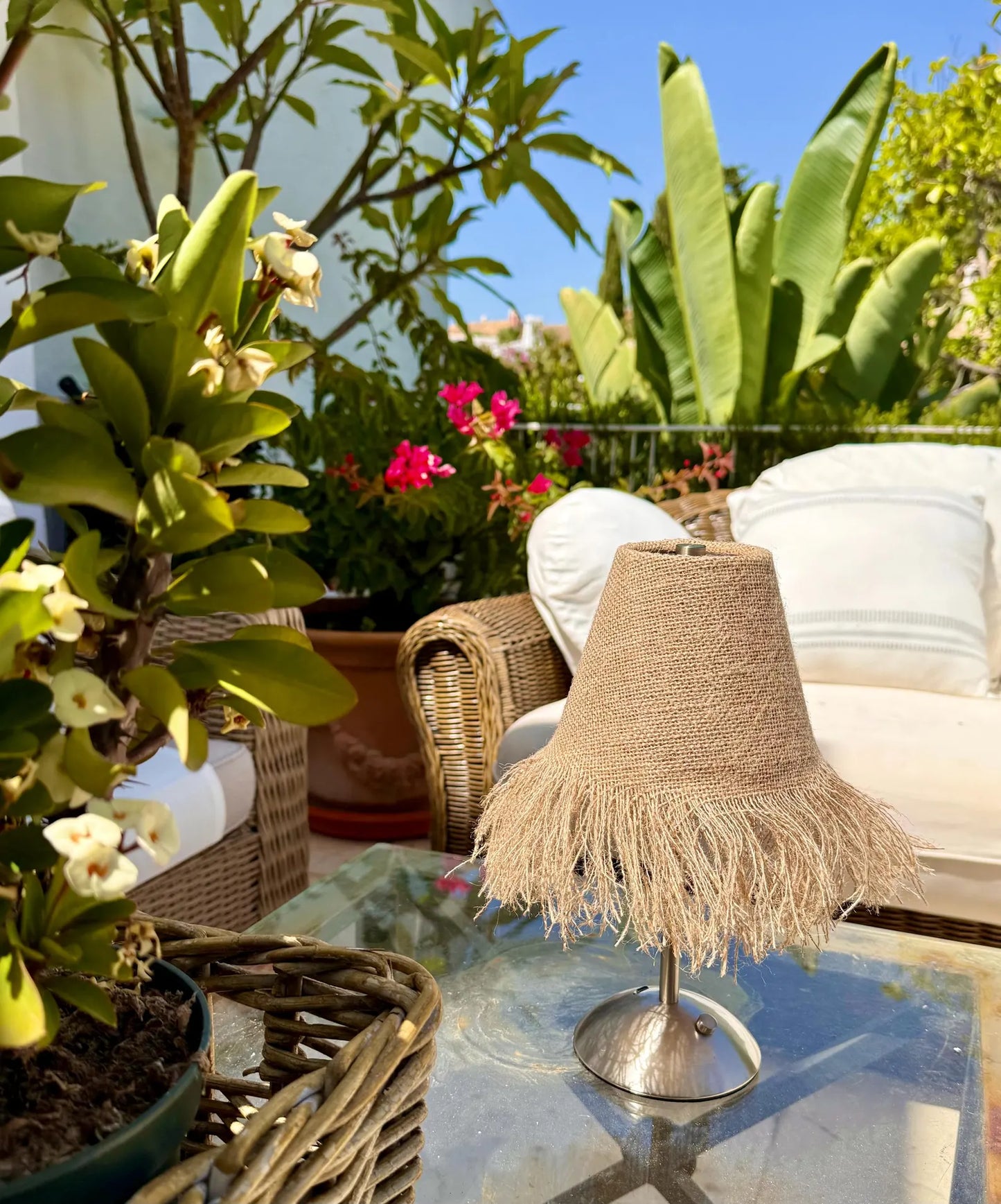 Handcrafted burlap fringe lamp shade on a cordless base styled outdoors with vibrant pink bougainvillea and lush tropical greenery.