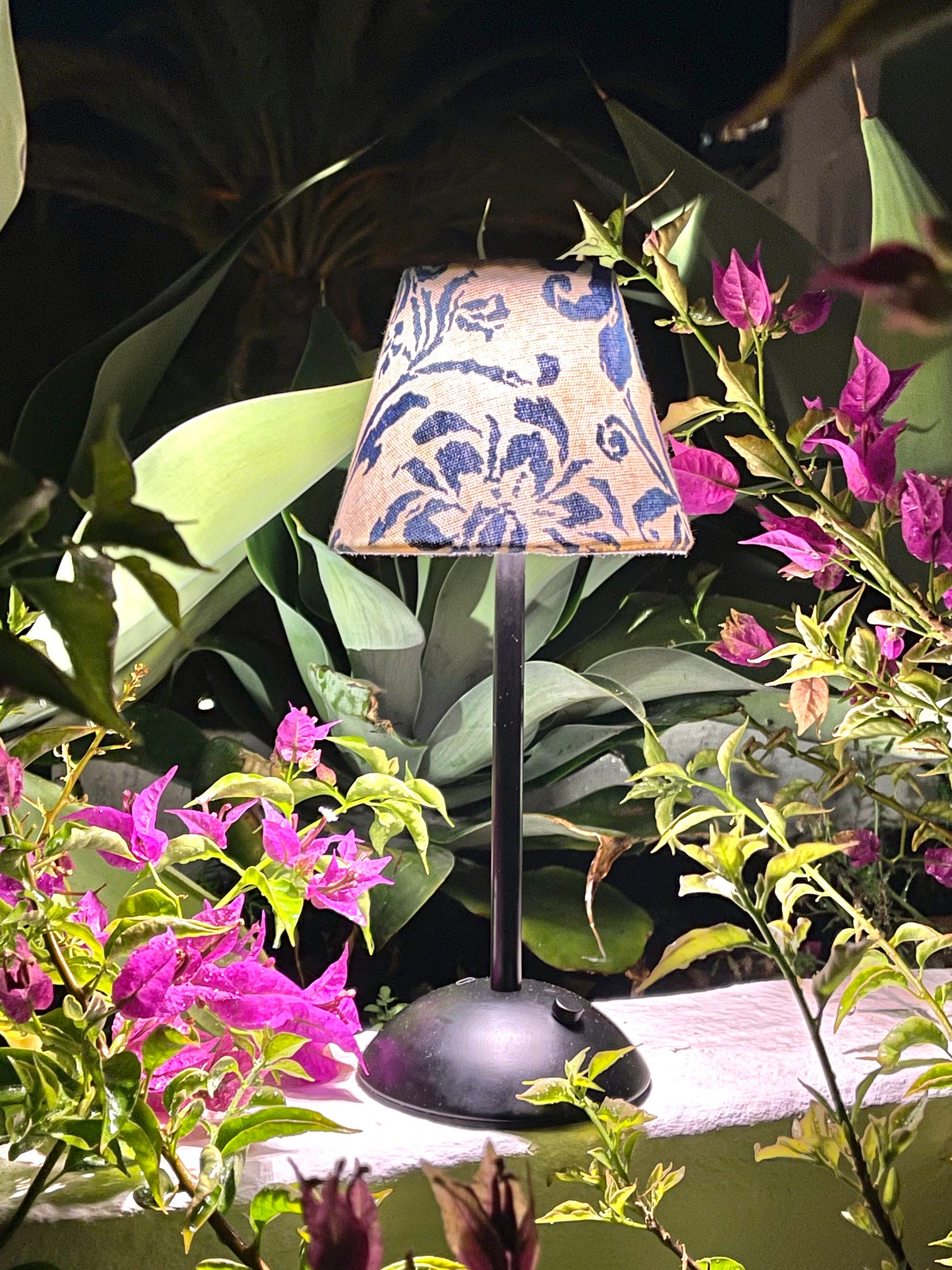 Lit Ralph Lauren blue floral shade on a black cordless lamp base styled outdoors with vibrant pink bougainvillea.