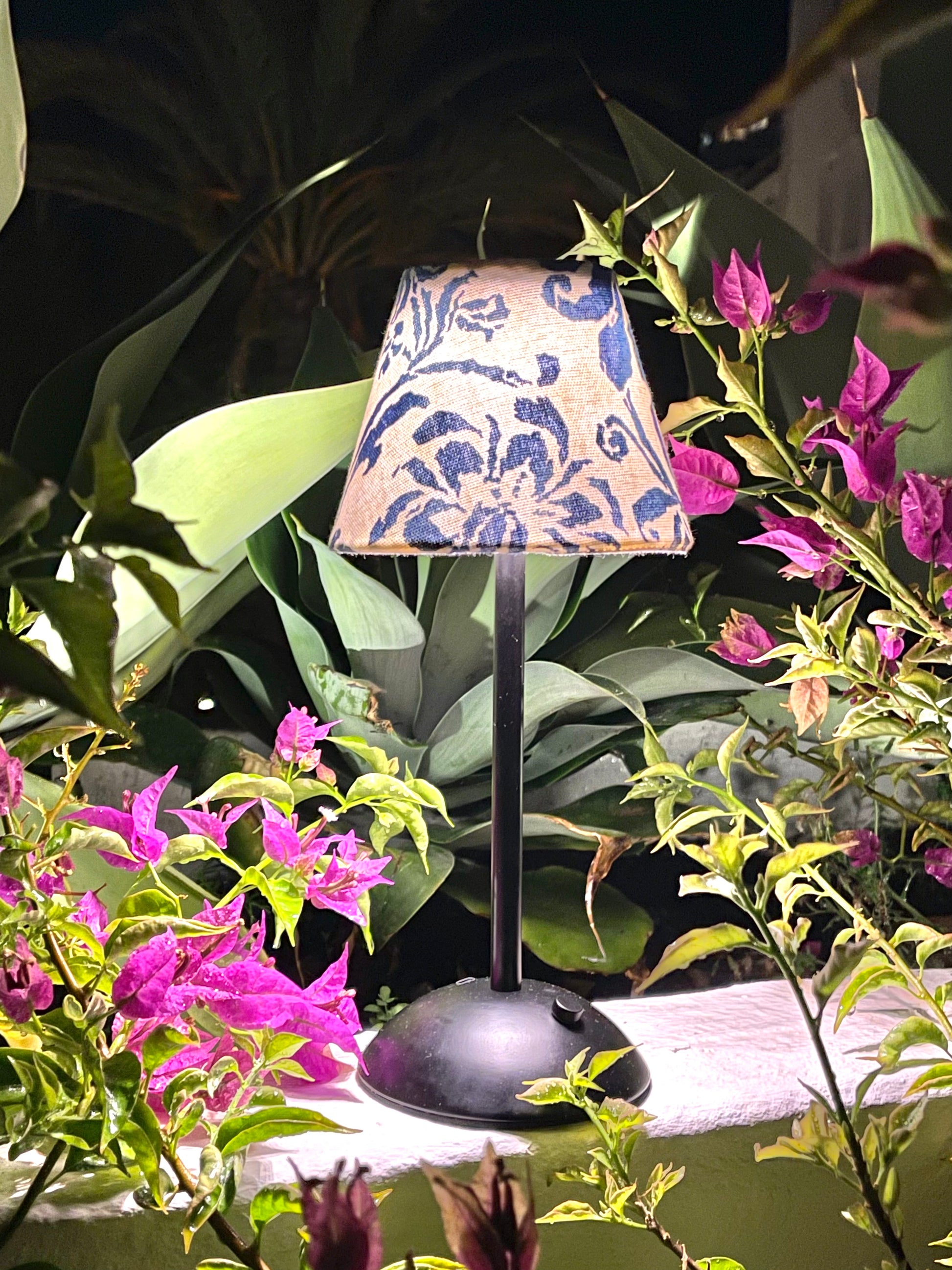 Lit Ralph Lauren blue floral shade on a black cordless lamp base styled outdoors with vibrant pink bougainvillea.