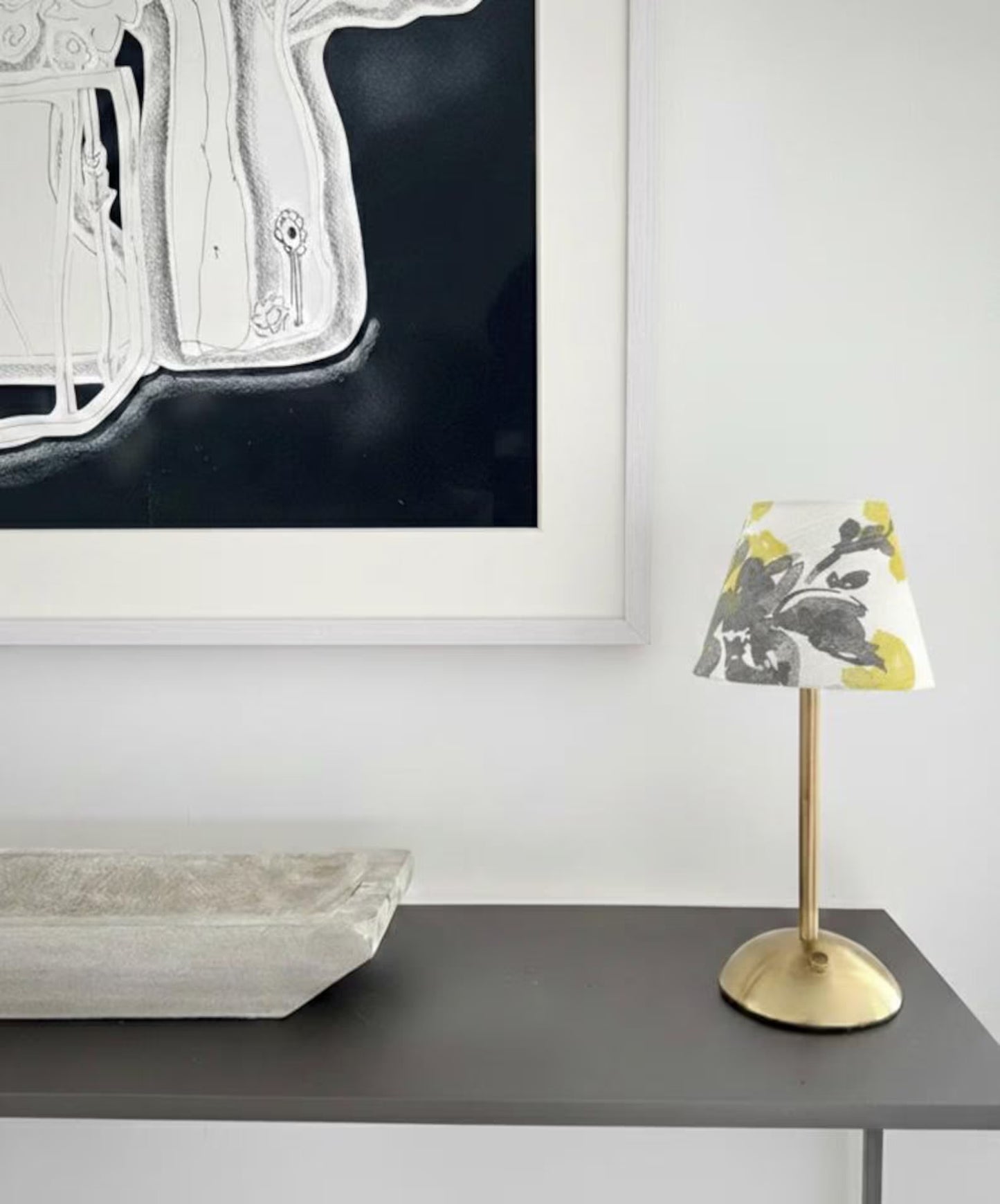 Small cordless table lamp with a decorative shade on a surface next to abstract art.